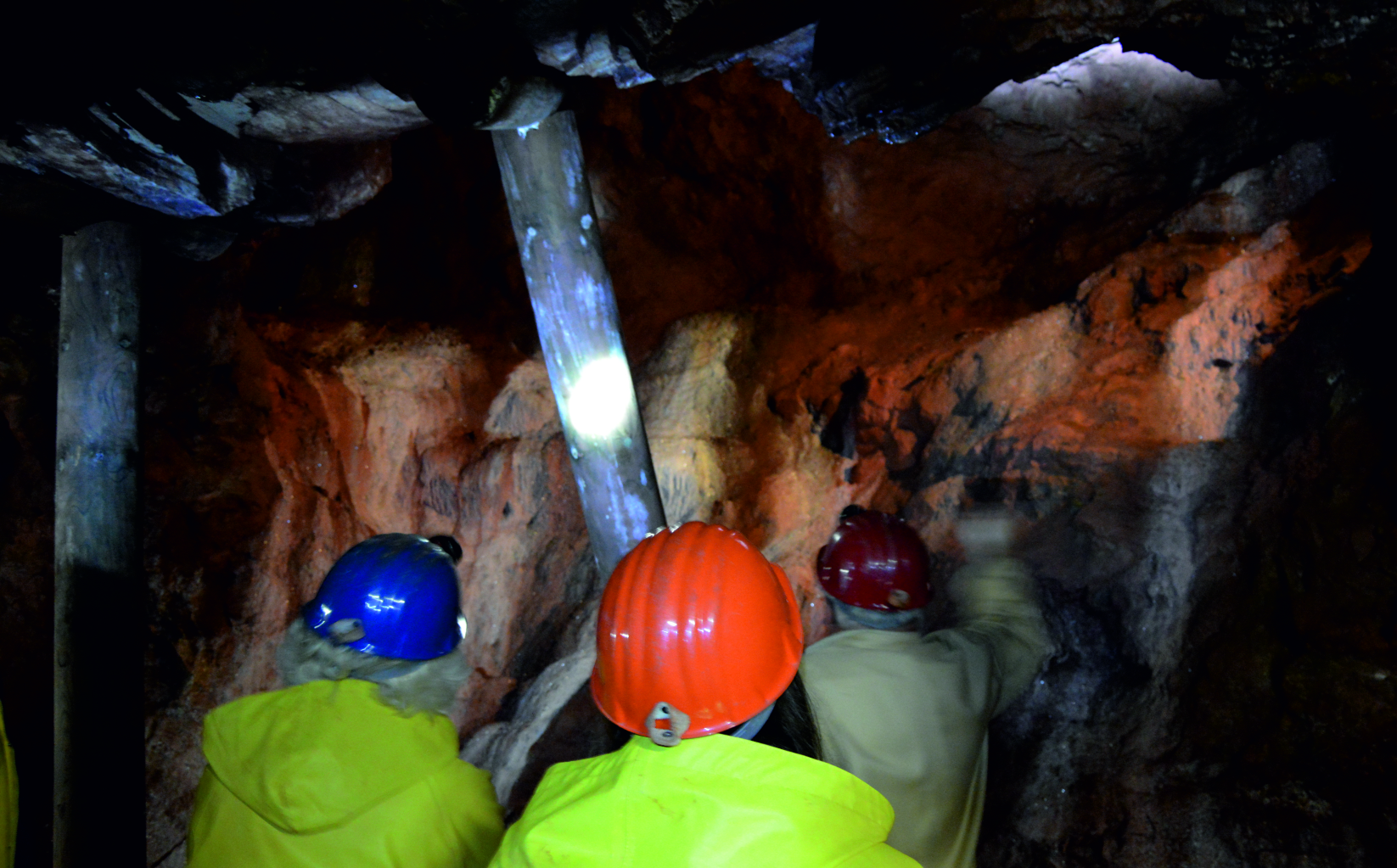 Das Bild zeigt eine Gruppe von Besucherinnen und Besuchern während einer Stollenführung im ehemaligen Bergwerk Grube Christiane in der Ferienregion Diemelsee. Alle Teilnehmenden tragen gelbe Schutzjacken und Helme. Sie in einem schmalen, beleuchteten Stollen mit feuchten Wänden und rustikalem Gestein. Die Szenerie vermittelt einen authentischen Eindruck vom früheren Arbeitsumfeld unter Tage und bietet einen spannenden Einblick in die Bergbaugeschichte der Region.