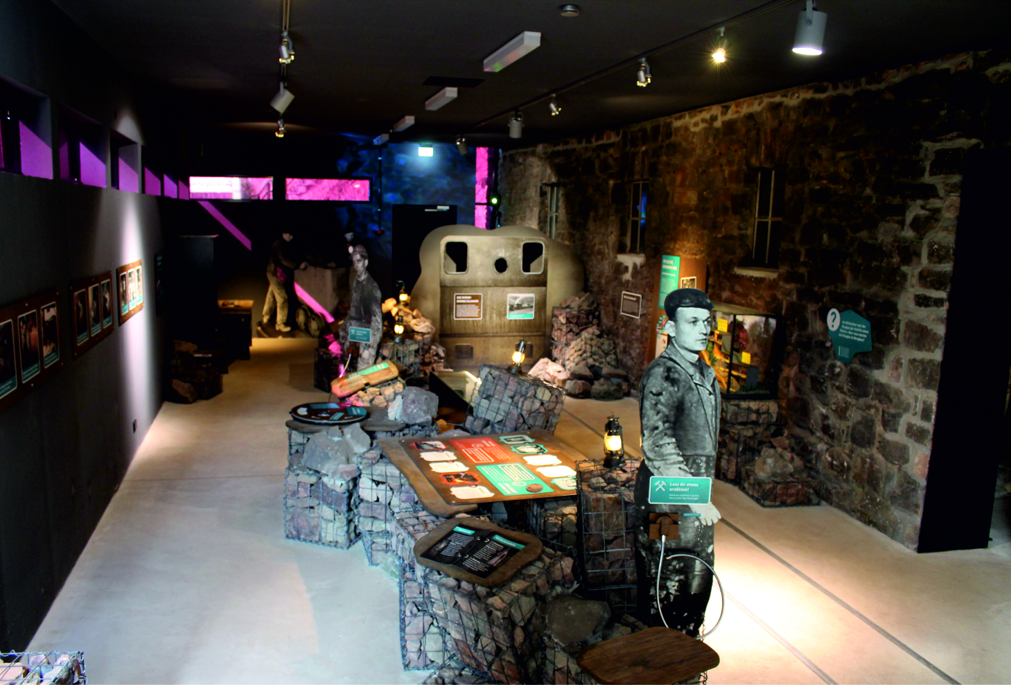 Das Bild zeigt eine moderne, interaktive Ausstellung im Info-Center des Besucherbergwerks Grube Christiane in Adorf. In einem hellen Ausstellungsraum stehen digitale Bildschirme, auf denen Besucher Informationen zur Geschichte des Bergwerks und zur Region abrufen können. Ergänzt wird das Angebot durch anschauliche Informationstafeln, historische Objekte und Mitmachstationen, an denen Kinder und Erwachsene spielerisch lernen können. Die Gestaltung ist modern, barrierearm und einladend – ein Ort, der Wissen über den Bergbau verständlich und spannend vermittelt.