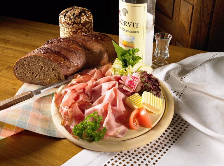 Das Bild zeigt eine rustikale Brotzeit in der Gastronomie am Diemelsee im Sauerland. Auf dem Tisch liegen eine vielfältige Wurstplatte, frisches Brot und eine Flasche Schnaps bereit. Die gedeckte Brotzeit spiegelt die regionale Küche und Gemütlichkeit wider, ideal zum Genießen nach einem Ausflug in die Natur.