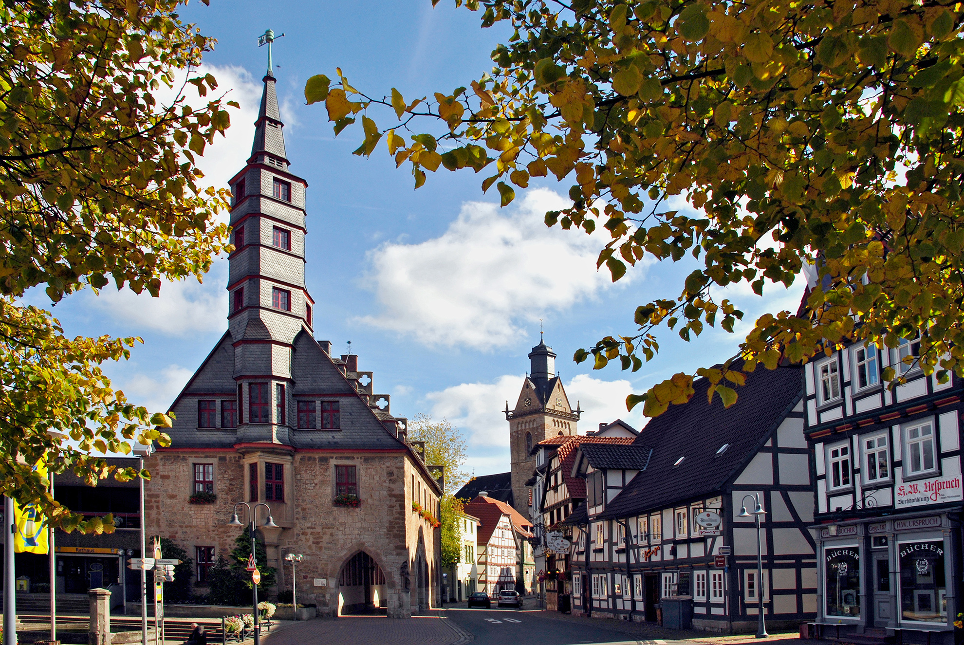 Blick auf die historische Altstadt von Korbach, der einzigen Hansestadt in Hessen. Im Vordergrund stehen das Rathaus und im Hintergrund die gotische Kilianskirche mit ihren markanten Türmen. Umgeben wird die Szene von grünen Bäumen. Typische Fachwerkhäuser mit verzierten Fassaden prägen das Stadtbild und vermitteln ein mittelalterliches Flair.