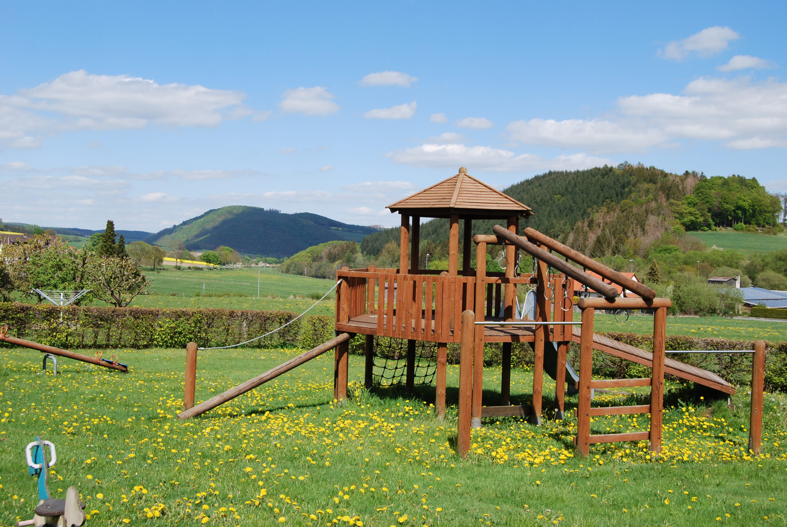 Mehrere Holzspielgeräte stehen auf einem Spielplatz in Stormbruch, umgeben von grüner Natur. Rund um das Spielgerät wachsen Bäume, Büsche und Sträucher, die dem Bereich eine naturnahe Atmosphäre verleihen. Das Spielgerät lädt Kinder zum Klettern und Spielen ein. Mehrere Holzspielgeräte stehen auf einem Spielplatz in Stormbruch, umgeben von grüner Natur. Rund um das Spielgerät wachsen Bäume, Büsche und Sträucher, die dem Bereich eine naturnahe Atmosphäre verleihen. Das Spielgerät lädt Kinder zum Klettern und Spielen ein.